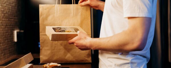 En man packar upp matlådor och råvaror från en papperskasse i ett kök.