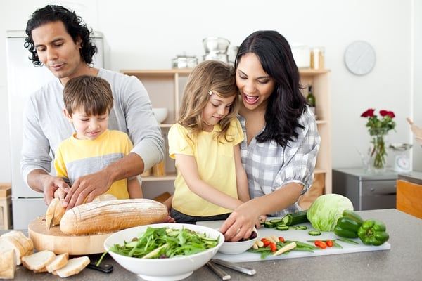 En familj förbereder hälsosamma grönsaker och bröd tillsammans i köket.