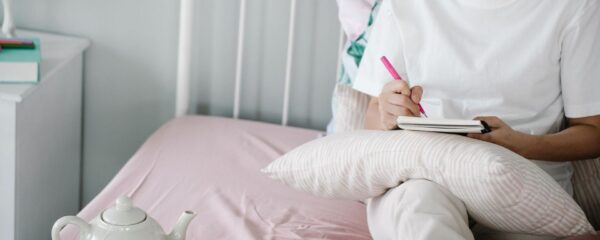 Person skriver i en anteckningsbok i en bäddad säng med te