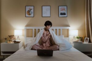 Person i pyjamas sitter i sängen med en öppen laptop på kvällen